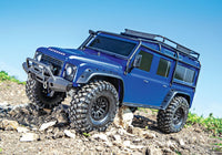 [Action] Traxxas TRX-4 Defender Combo - Mavi Defender mavi gökyüzü altında topraklı arazide ön-sol açı