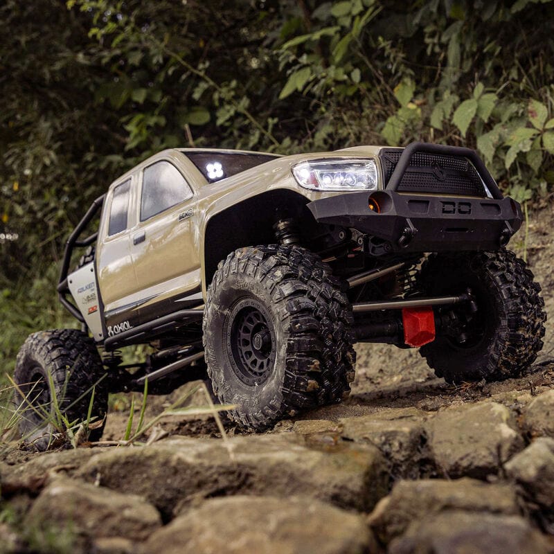[Action] Axial SCX6 Trail Honcho - kum rengi araç ormanlık kayalık arazide arkadan görünüm