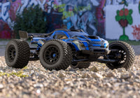 [Action] Traxxas XRT 4WD - mavi araç grafitili duvar önünde arazi zemininde